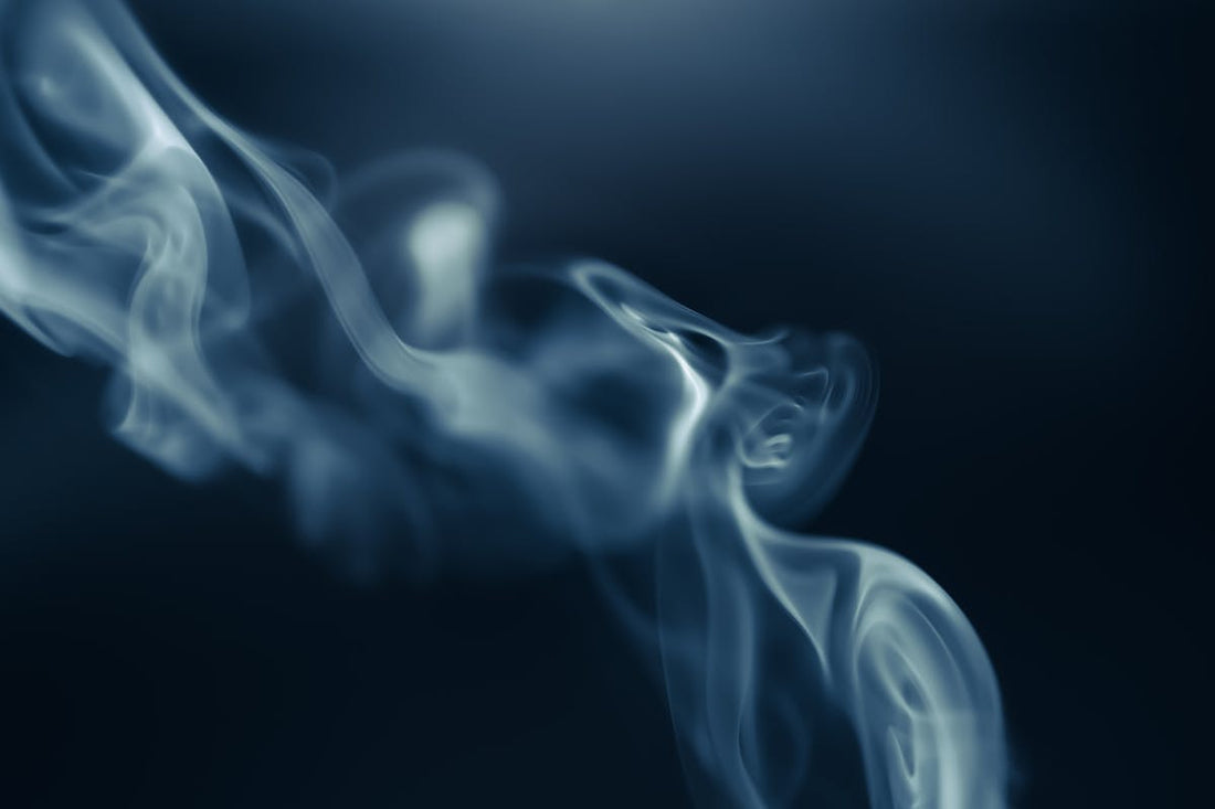 White smoke drifting through a dark blue background, evoking the sillage of a high-quality men's fragrance