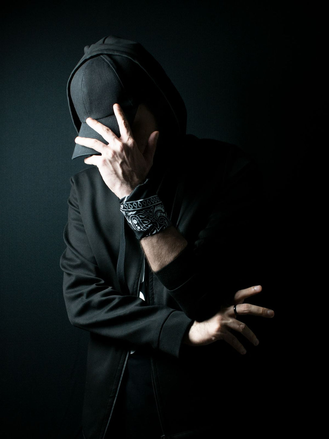 Man in a black hoodie and cap against a dark studio background
