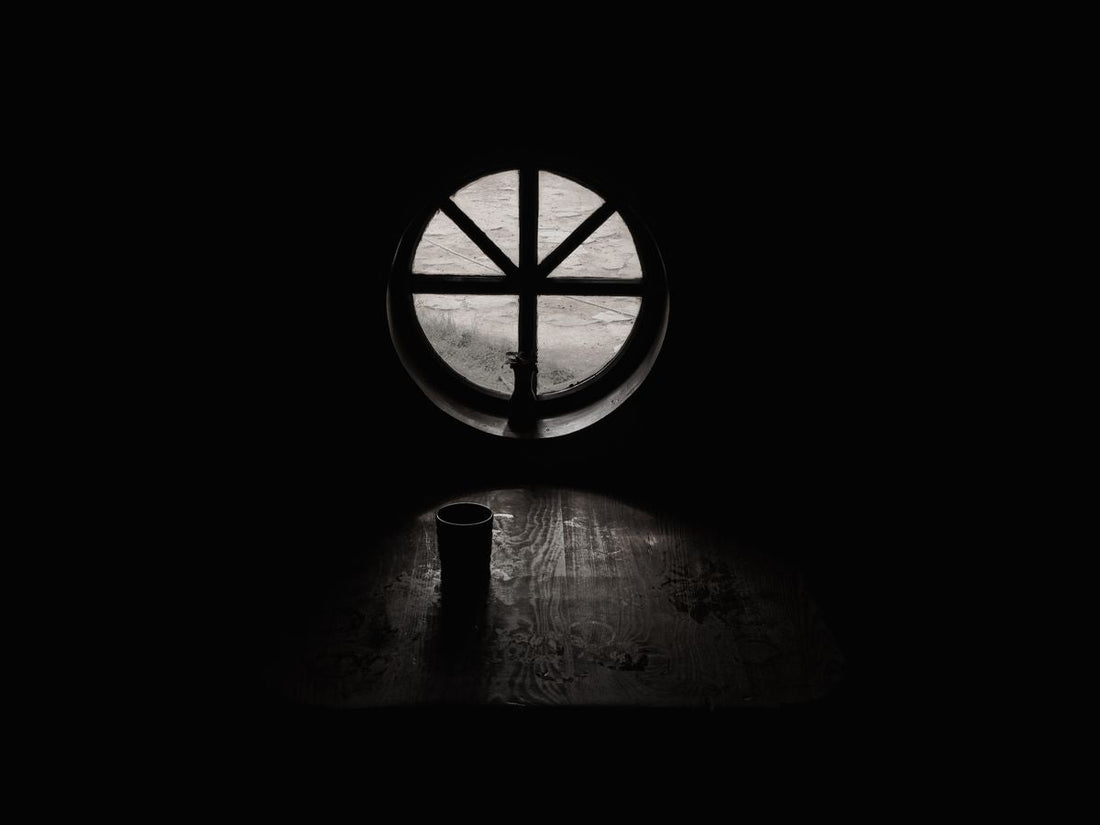 Grayscale cup of coffee beside a bright window in a bare, quiet room