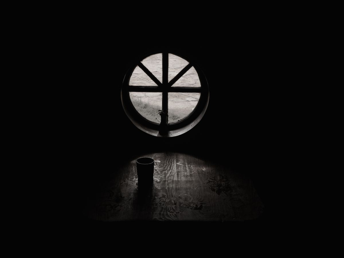 Grayscale cup of coffee beside a bright window in a bare, quiet room