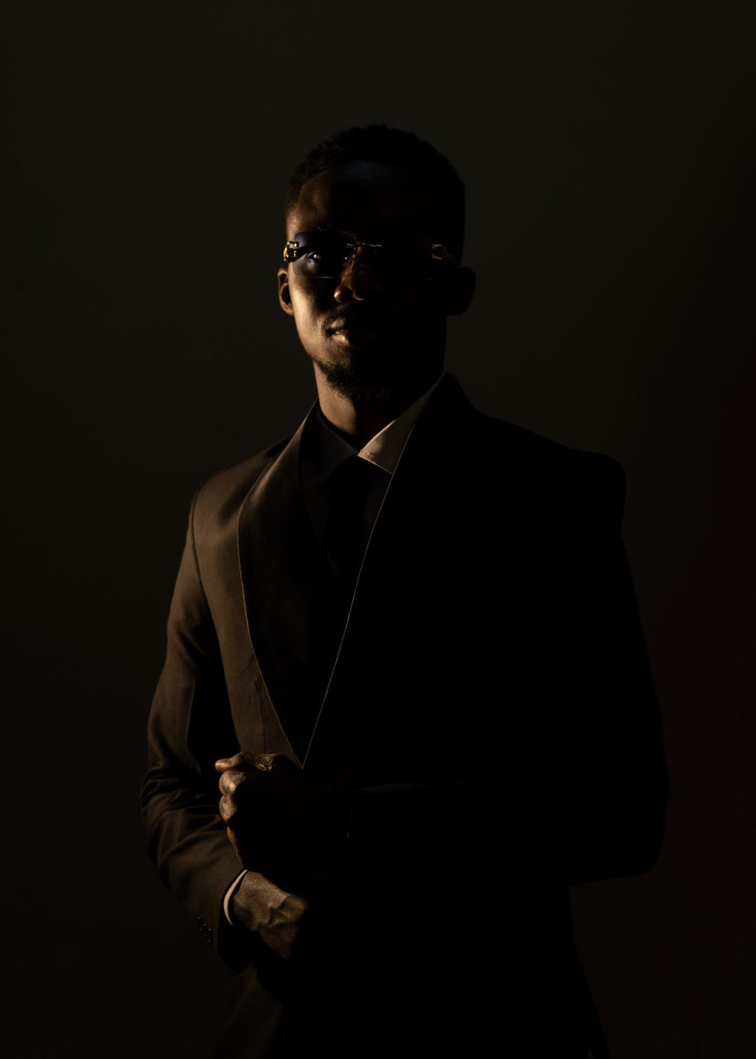 Man in a dark suit lit against shadow, composed and silent, editorial portrait