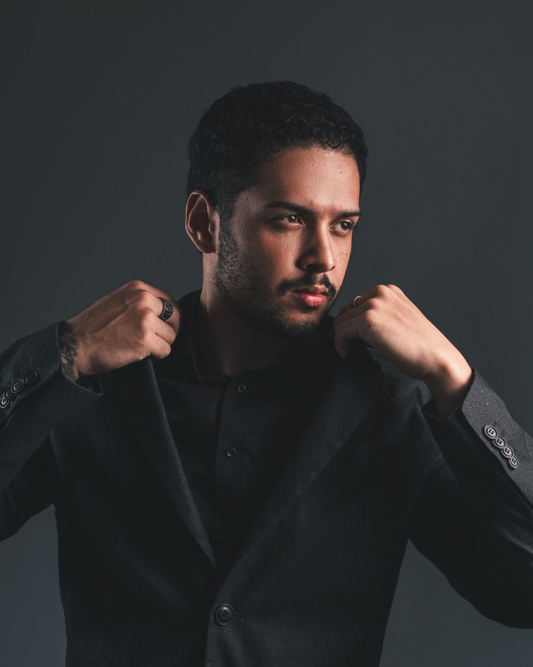 Man in a dark tailored suit adjusting his jacket in a studio