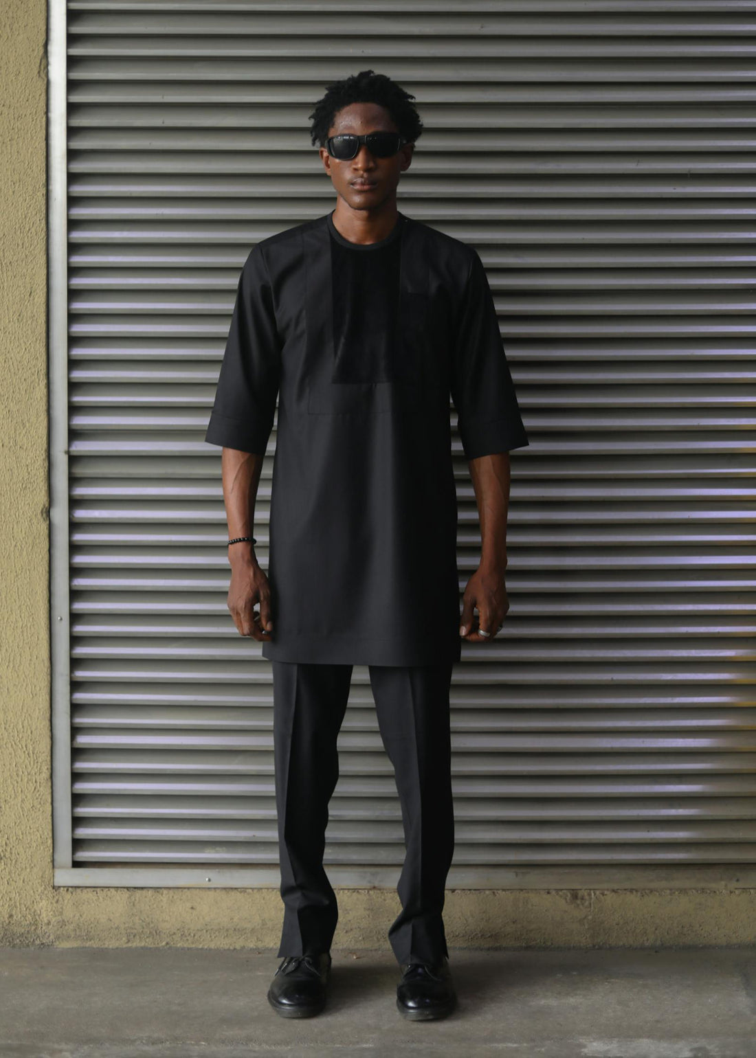Man in a sharp black outfit and sunglasses against a dark backdrop