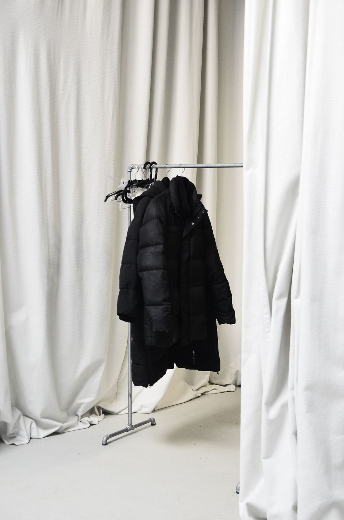 Black wool coat hanging alone on a silver clothing rail in daylight
