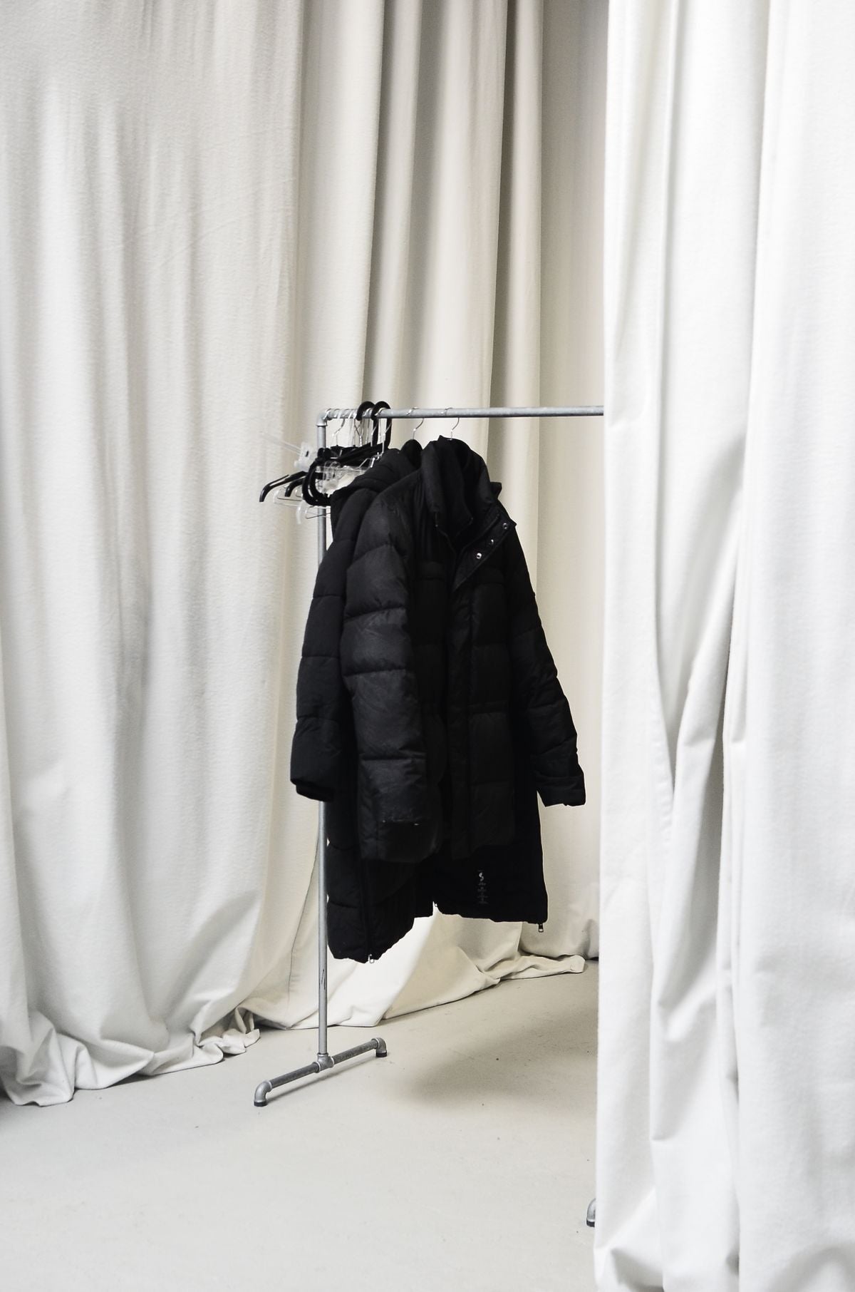Black wool coat hanging alone on a silver clothing rail in daylight