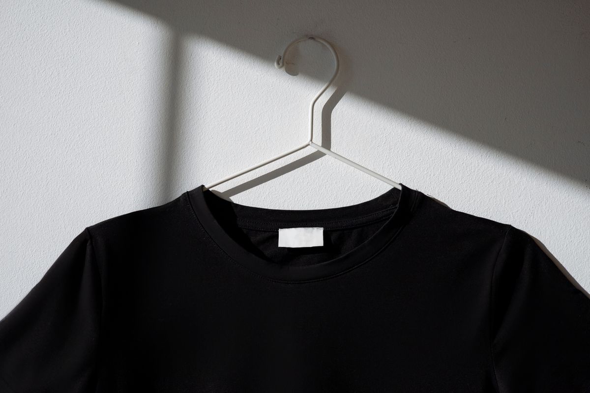 A single black shirt hanging against a plain dark wall, minimalist and premium.