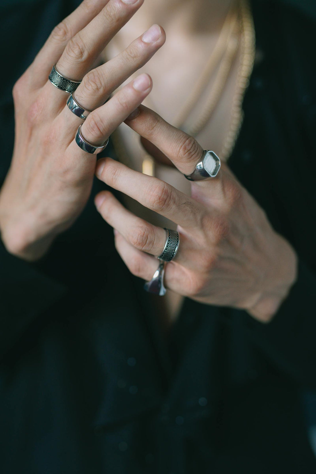 Close-up of a man's hands wearing multiple silver and signet rings on a dark background
