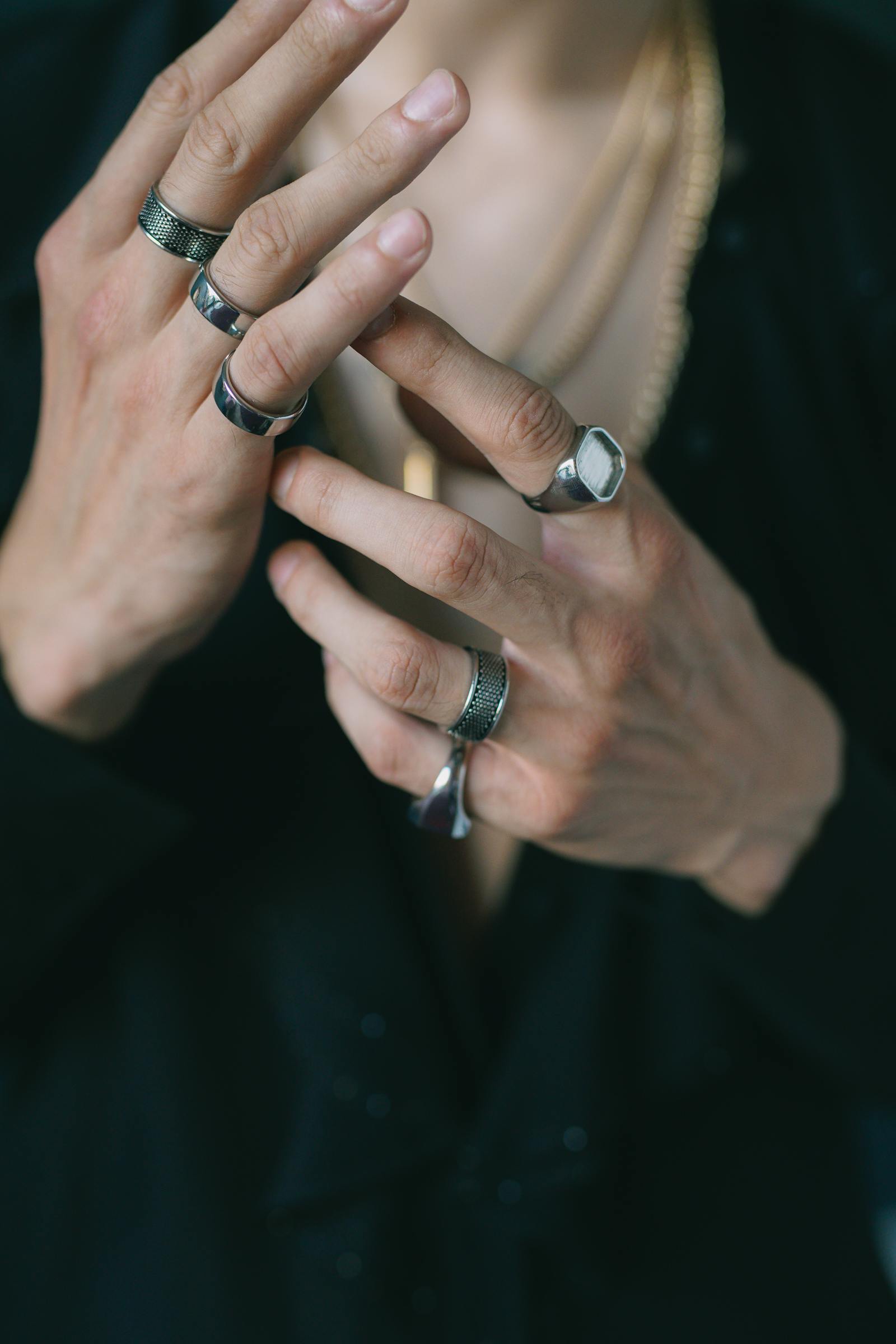 Close-up of a man's hands wearing multiple silver and signet rings on a dark background