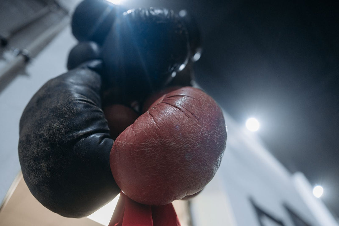 Two worn leather boxing gloves hanging together in a dark gym